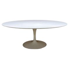 an oval dining table with a white top and silver base, against a white background