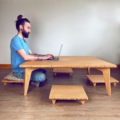 a man sitting at a wooden table with a laptop on his lap and stools in front of him