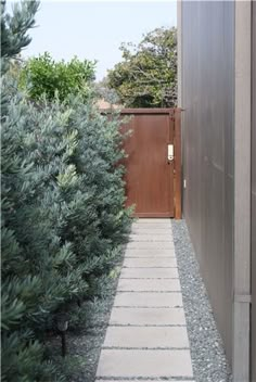 a narrow walkway between two trees in front of a building with a wooden fence and gate