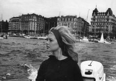 a woman riding on the back of a boat down a river next to tall buildings