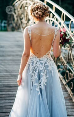 a woman walking across a bridge wearing a blue dress with white lace on the back