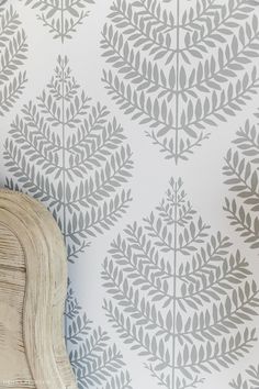 a white chair sitting next to a wall with grey leaves on it