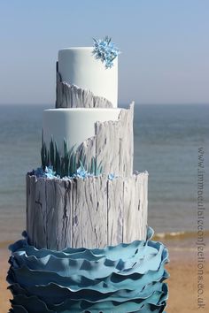 a three tiered cake sitting on top of a wooden table next to the ocean