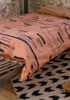 a bed with an orange comforter on top of it next to a black and white rug