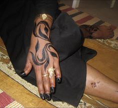 a woman's hand with tattoos on it sitting on the floor next to a rug