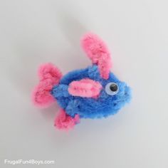 a blue and pink stuffed animal with big eyes on it's face, sitting on a white surface