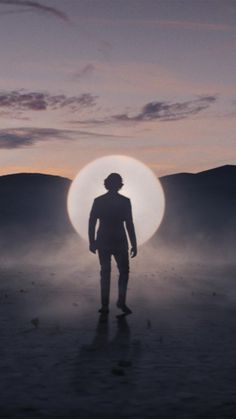 a man standing in the middle of a desert at night with a large round object behind him