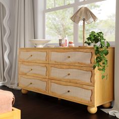 a wooden dresser sitting in front of a window next to a potted green plant