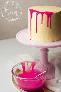 a cake with pink icing sitting on top of a table next to a bowl