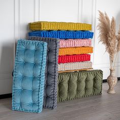 a stack of blankets sitting on top of a wooden floor next to a vase filled with dry grass