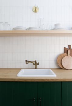 a white sink sitting under a wooden shelf next to a green cabinet and counter top