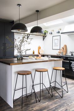 a kitchen with three stools and an island in the middle, surrounded by black cabinets