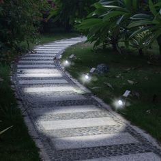 a path made out of stones with lights shining on the walkway and trees in the background