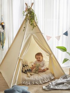 a baby sitting in a teepee with a teddy bear and stuffed animal on the floor