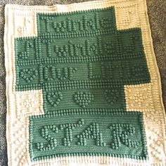 a green and white crocheted blanket on the floor with words written across it