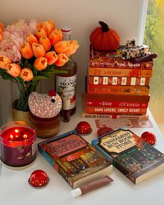 a table topped with books and candles next to a vase filled with orange tulips