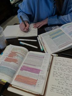 a person sitting at a table with several books and writing utensils on it