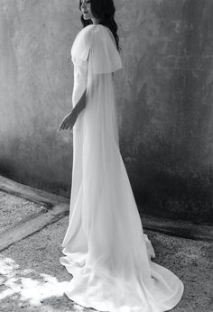 black and white photograph of woman in wedding dress with veil on her head, leaning against wall