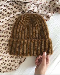 a hand is holding a brown knitted hat on top of a white bed sheet