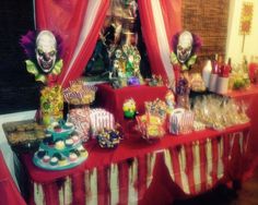 a red table topped with lots of candy and skulls next to a window covered in curtains