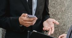 two men in suits are looking at their cell phones