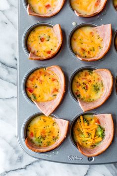 an open muffin tin filled with eggs and ham on a blue tablecloth next to a white plate