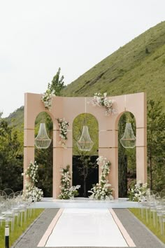 an outdoor ceremony setup with white flowers and chandeliers on the aisle, surrounded by greenery