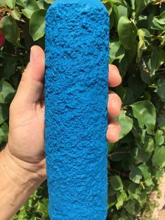 a hand holding a blue cylinder in front of some flowers