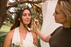 a woman is getting her make - up done by another woman in front of a tree