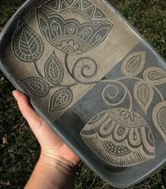 a person holding a metal tray with an owl design on it's side in the grass