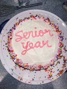 a white cake with pink frosting and sprinkles on it that says senior year