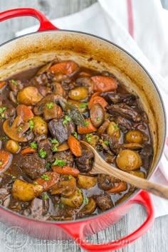 a red pot filled with stew on top of a wooden table