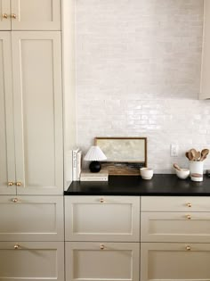 a kitchen with white cabinets and black counter tops in front of a brick backsplash