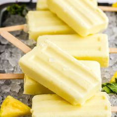 four popsicles on top of ice with pineapples and mint leaves in the background