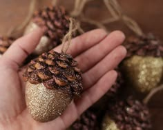 a hand holding a pine cone ornament in front of some gold glittered ornaments