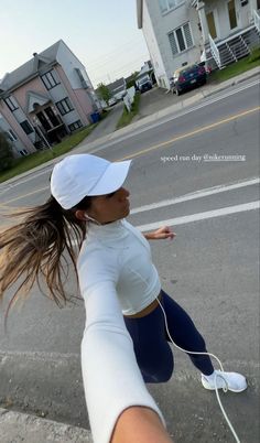 a woman is running down the street with headphones in her ears and wearing a white hat