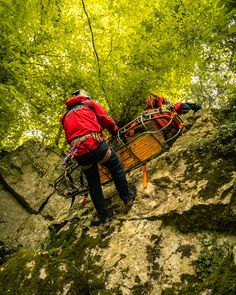 a man climbing up the side of a mountain in red jacket and black pants with harness on