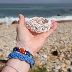 a hand holding a piece of rope with beads on it near the ocean and rocks