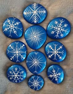 six blue painted rocks with white dots and snowflakes on them, arranged in a circle