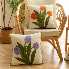 three pillows with flowers on them sit in front of a wicker chair and potted plant