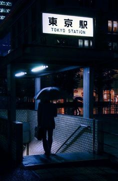 a person with an umbrella is walking down the street at night in tokyo station, japan