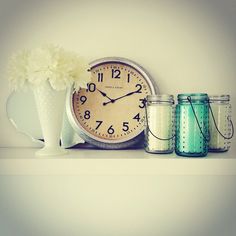 a clock sitting on top of a shelf next to two jars with flowers in them