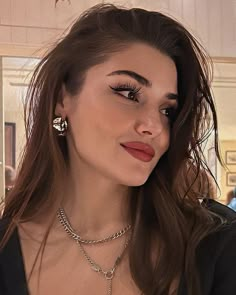 a woman with long brown hair wearing a necklace and earrings