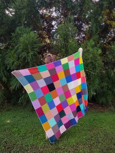 a person standing in the grass holding up a colorful blanket that is made to look like squares