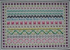 a close up of a cross stitch pattern on a white cloth with pink, green and yellow stitches