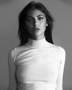 a black and white photo of a woman wearing a turtle neck sweater with her hands on her hips