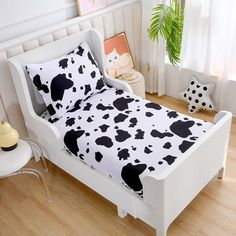 a white bed with black and white cow print sheets on it, next to a potted plant