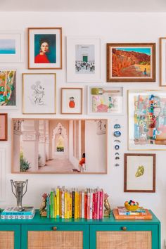 a wall full of framed pictures and books on top of a blue dresser next to a green cabinet