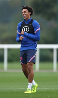 the soccer player smiles as he runs on the field with his arms crossed and feet apart