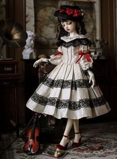 a doll dressed in white and black with a red bow standing next to a violin